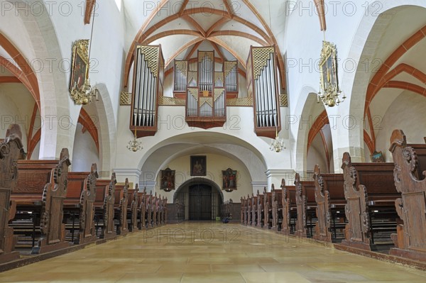 Interior of a church with detailed wooden benches and an impressive organ on the ceiling, St