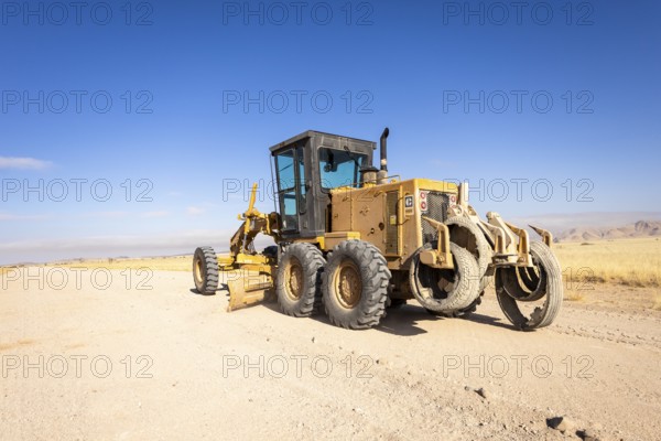 In the remote desert near Solitaire, Namibia, a tractor levels a dirt road across golden sand dunes