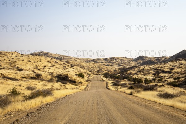 A road Spreetshoogte Pass in Namibia, with a gravel road winding through golden grassland and rocky