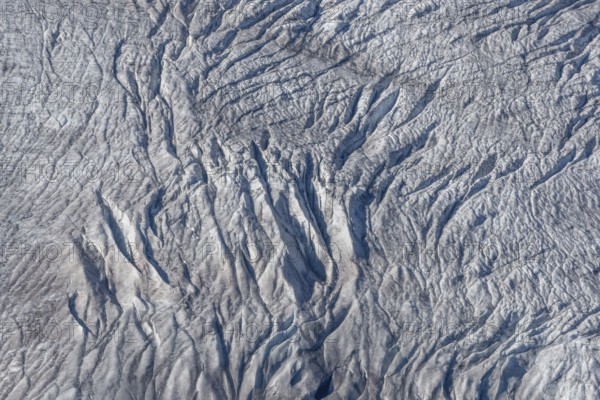 Crevasses and streaks mark the surface of the glacier. The sunlight highlights these unique