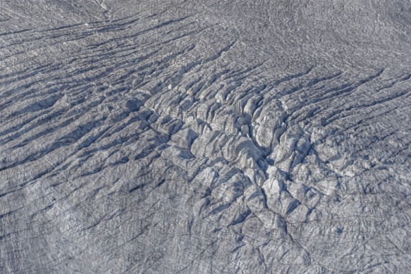 Crevasses and streaks mark the surface of the glacier. The sunlight highlights these unique