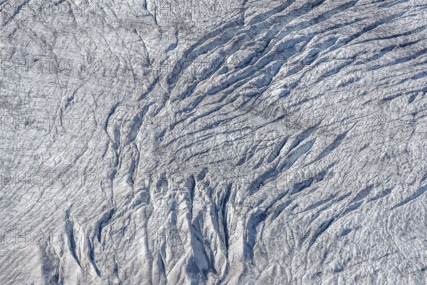 Crevices mark the surface of the glacier. The landscape is illuminated by daylight, highlighting