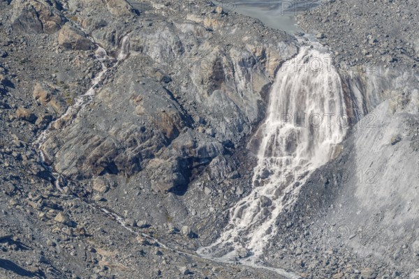 Waterfalls flow over a glacier surrounded by rocks and debris. This natural phenomenon is caused by