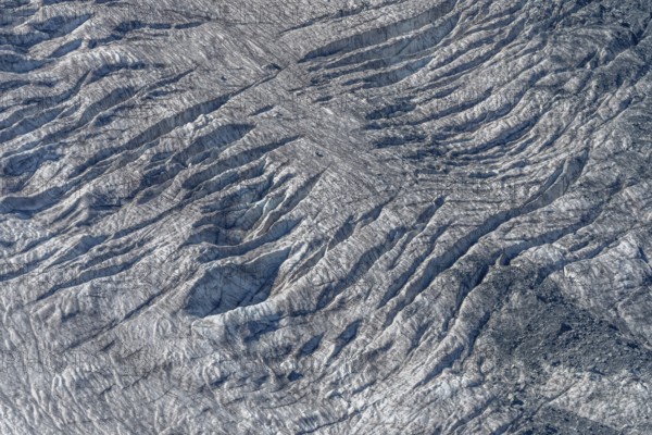 Crevices mark the surface of the glacier. The landscape is illuminated by daylight, highlighting