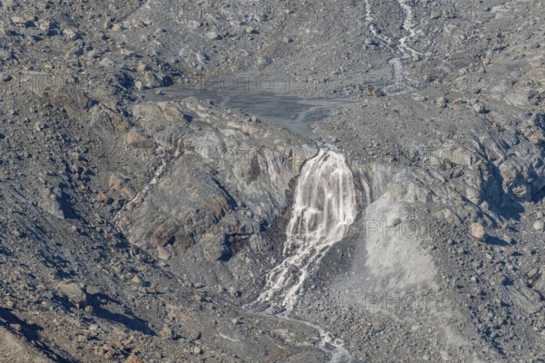 Waterfalls flow over a glacier surrounded by rocks and debris. This natural phenomenon is caused by