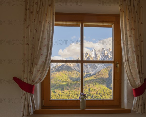 View through a window to the Dolomites in the foreground a small vase with meadow flowers on the