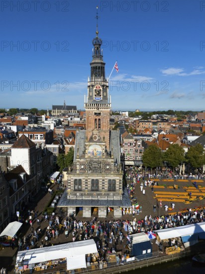 Imposing clock tower with lively market activity and market stalls in the foreground, under blue