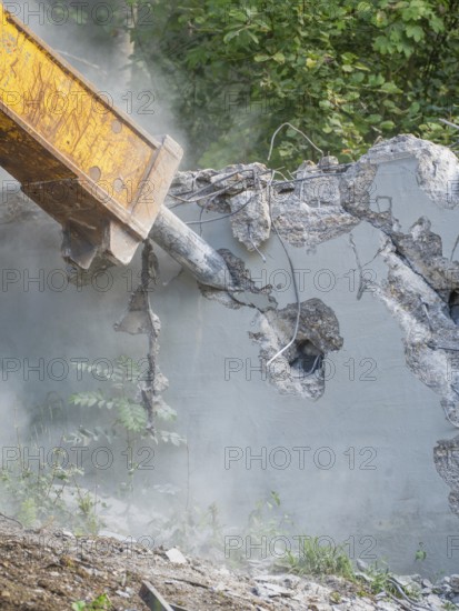 Close-up of a demolition hammer smashing concrete, surrounded by dust and plants, bridge