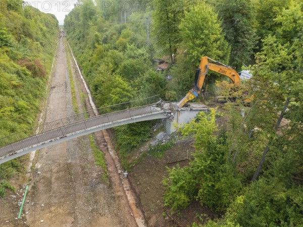 Bird's eye view of an excavator demolishing a bridge in the middle of the forest, with an empty