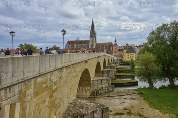 People walking across a historic bridge with a view of the cathedral and trees, Stone Bridge,