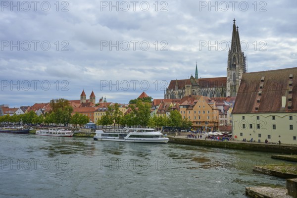 View of a cathedral and boats on a riverbank on a slightly cloudy day, Danube, Regensburg, Bavaria,
