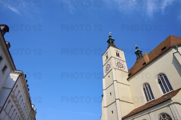Gothic-style church tower and building under a bright blue sky, flanked by other buildings,