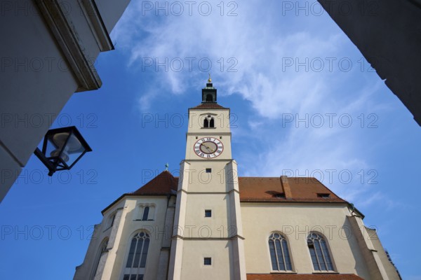 View of a high church tower with a clock under a bright blue sky, flanked by buildings,