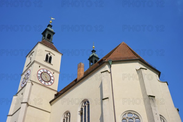 Close-up of a church tower with clock and red tiled roofs against a deep blue sky, Neupfarrkirche,
