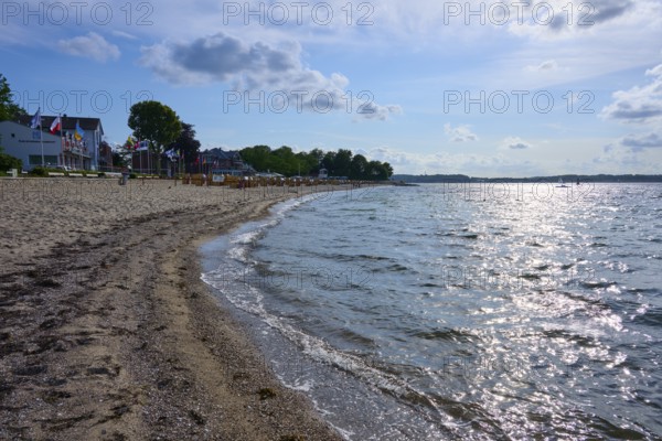 Sandy beach beach with undulating sea under a blue sky, the sun reflected on the water, Heikendorf,