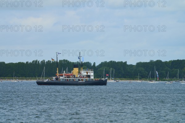 Icebreaker Stettin on a calm sea with several sailing boats and a cloudy sky, Windjammer Parade