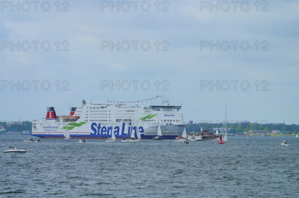 Large Stena Line ferry on the sea, surrounded by smaller sailing boats under a cloudy sky,