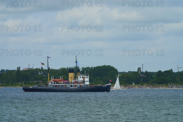 Historic icebreaker Stettin and a small sailing boat in front of a green coastal landscape and