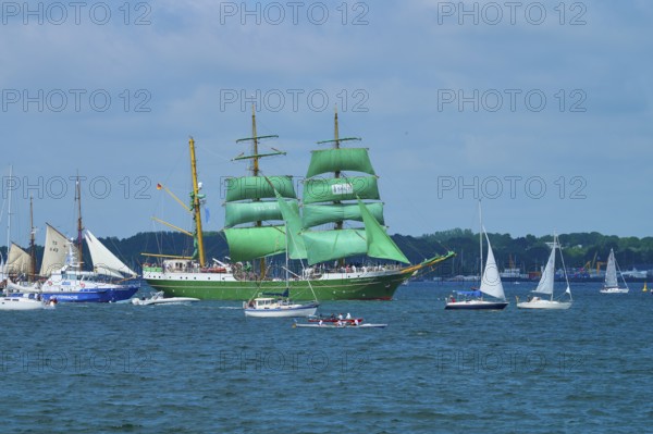 A large sailing ship with green sails Alexander von Humbold 2 and a group of smaller boats on the