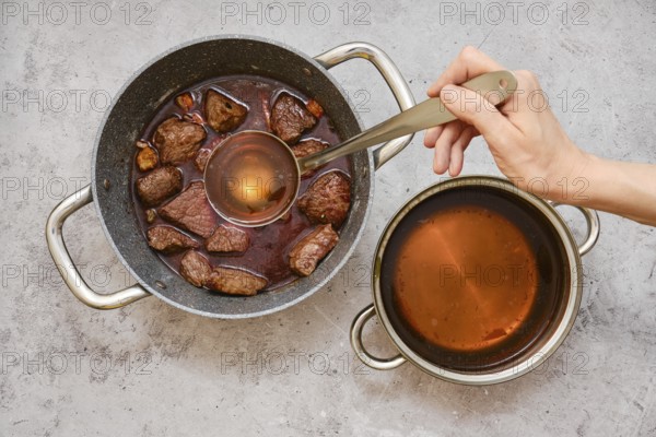 A person is using a ladle to add beef broth to a pot filled with fried chunks of beef shoulder and