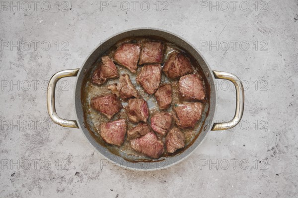 Chunks of beef are sizzling in a frying pan, showcasing a delicious golden-brown crust in the