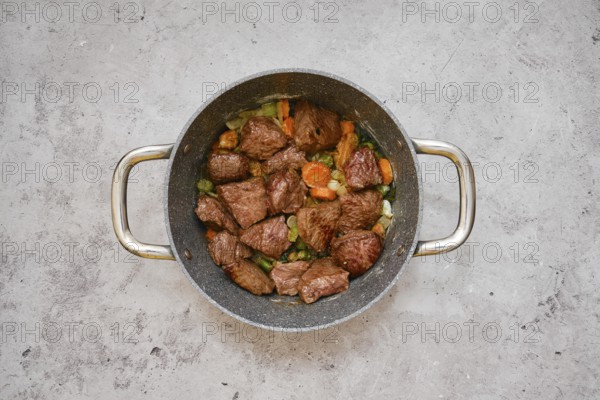 Tender pieces of beef are simmering with a mix of carrots, celery, and onions in a cooking pot. The