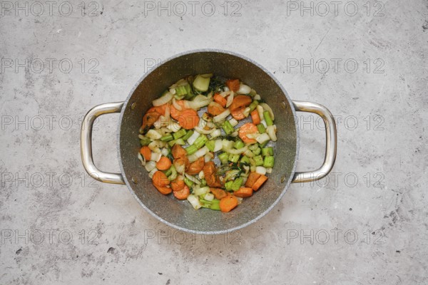 Chopped carrots, celery, and onion are frying in a pot, creating a vibrant vegetable base mixture