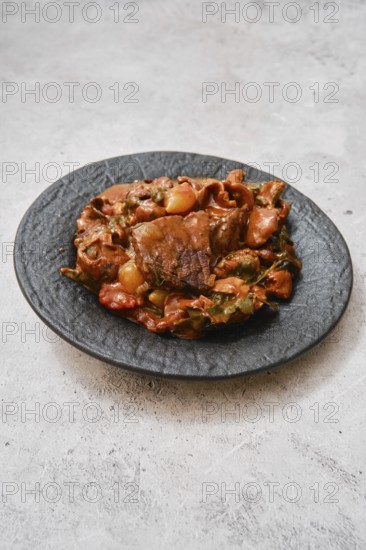 A hearty meat stew is presented on an elegant black plate. The dish features tender chunks of beef