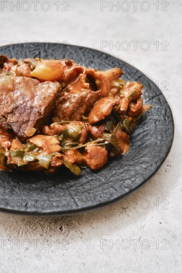 A flavorful combination of tender meat and a medley of vegetables on a black plate. The dish