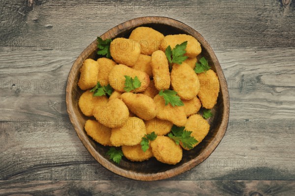 A generous serving of golden chicken nuggets is arranged in a rustic wooden bowl, garnished with