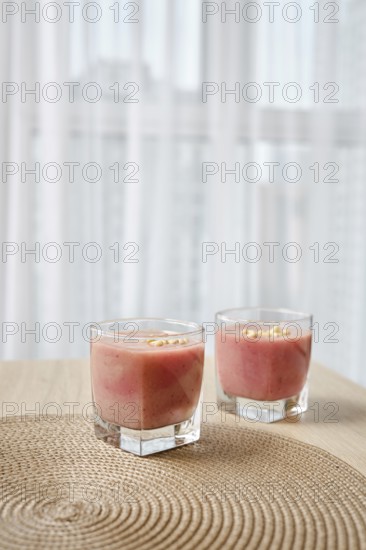 Two elegant glasses filled with a vibrant banana-strawberry smoothie sit atop a woven placemat on a