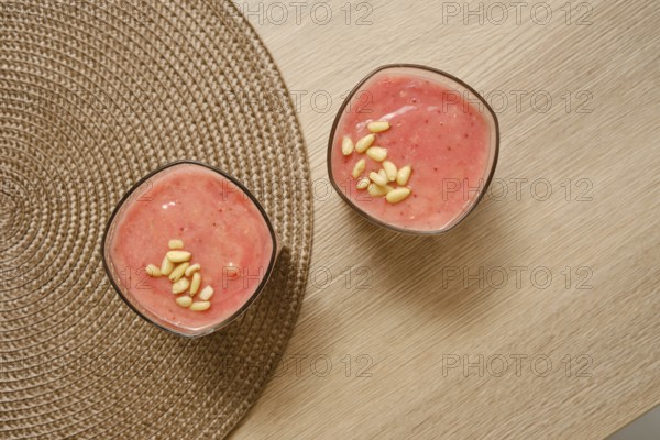 Two glasses filled with a creamy banana-strawberry smoothie sit on a natural-colored table. Topped
