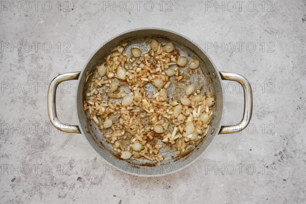A silver pan contains a mixture of caramelized pearl onions and chopped shallot, creating a savory