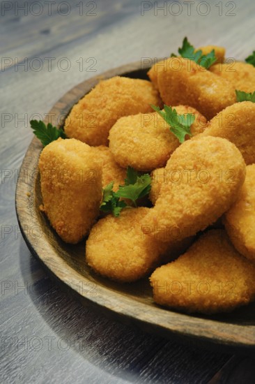 Close-up view of golden-brown chicken nuggets in breading on a rustic wooden platter. The crispy