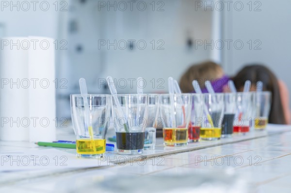 Glasses with different coloured liquids and pipettes arranged for a laboratory experiment, Youth