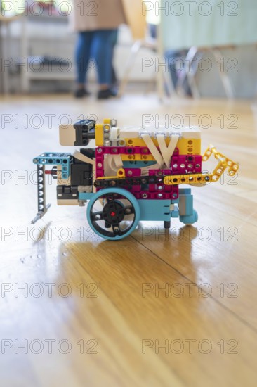 Colourful Lego robot with wheels on a wooden floor demonstrates technical creativity, Youth