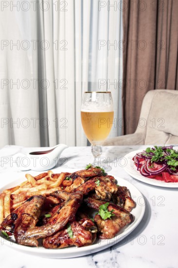 Delicious barbecue chicken wings, with French fries, salad and a refreshing drink, at a cozy table,