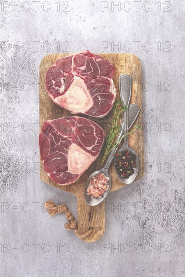 Freshly sliced beef legs, two ossobuco steaks, on a wooden board, with spices and herbs, ready to