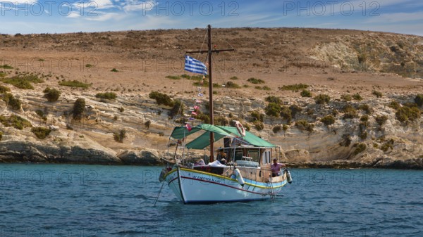 A boat with a Greek flag sails along rocky shores, the sea is blue and calm, White Cliffs, White