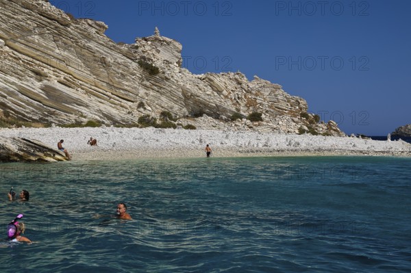 People swimming in calm turquoise waters off a rocky coast, White Cliffs, White Beach, Makri