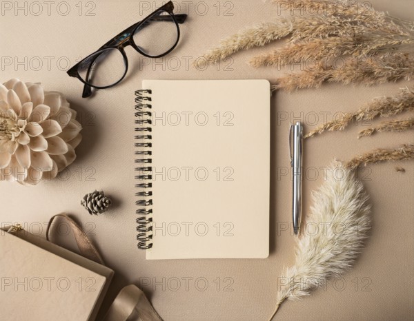 Flat lay composition featuring a beige spiral notebook, elegant pen, glasses, dried flowers, and