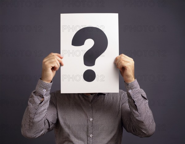 A person concealing their face while holding a question mark sign, symbolizing anonymity, mystery,