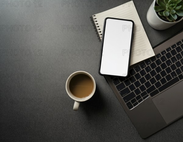 Op view of an organized workspace featuring a laptop, smartphone, notebook, pen, plant, and coffee