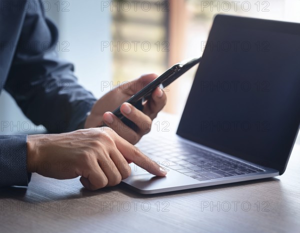 A man in a professional office environment multitasking with a smartphone and laptop, conveying