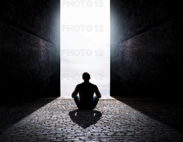 Silhouette of a person sitting alone within a brick archway, observing a peaceful and scenic cloudy