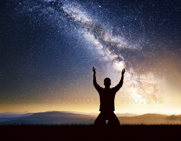A man kneels in peaceful reflection under the vibrant Milky Way galaxy at sunset in an open natural