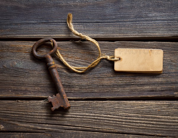 A close-up of an ornate vintage key with a blank label attached, resting on a brown surface under