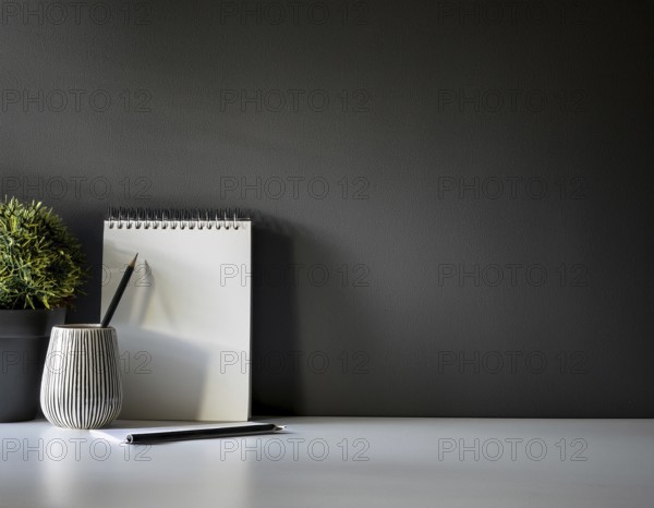 A clean and modern office workspace featuring a pen holder, notebook, and ceramic vase against a