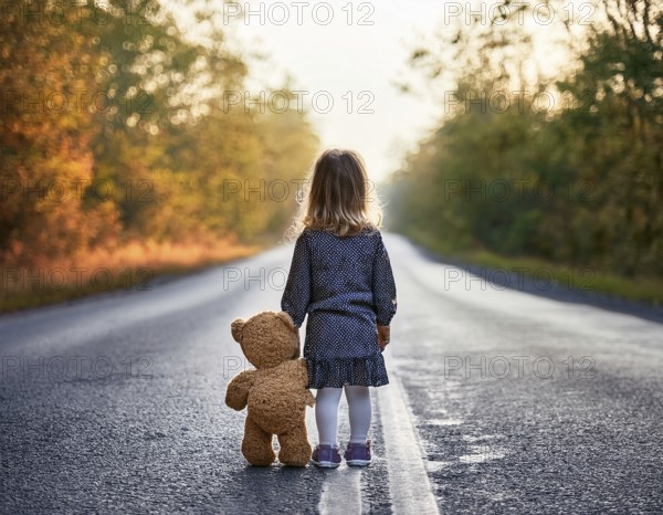 A young child stands alone holding a teddy bear in an urban outdoor setting, symbolizing innocence