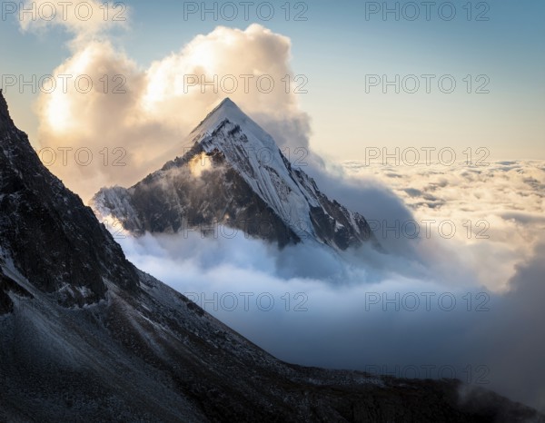 A stunning view of a snowy mountain peak rising above the clouds, with a blue sky background.